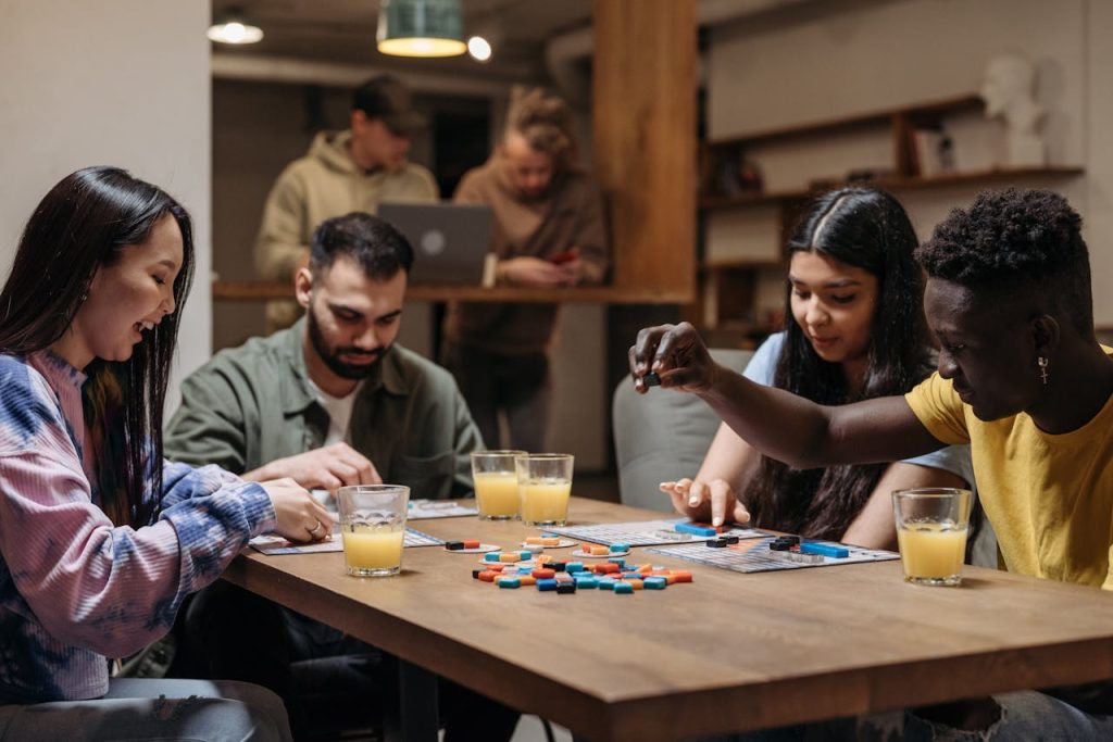 A diverse group of friends playing board games with drinks, socializing indoors.
